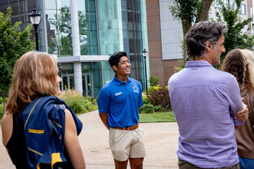 A student tour guide leads visitors past academic buildings during a campus tour