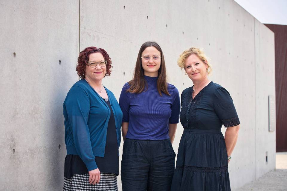 Three women stand in front of a stone wall Three women stand in front of a stone wall