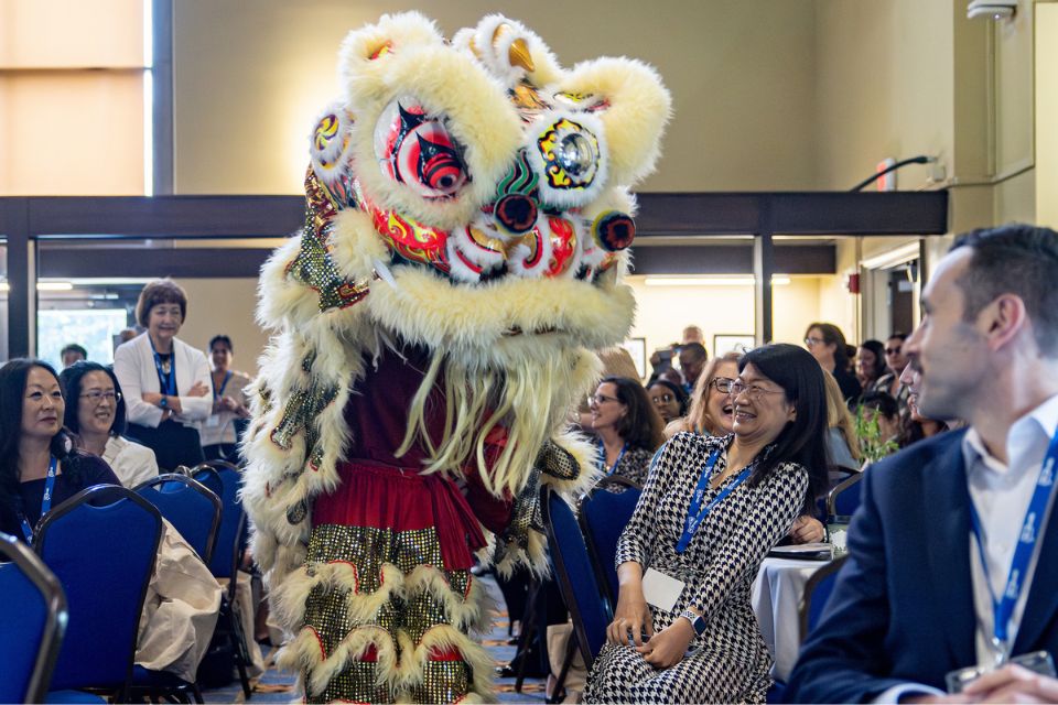 Audience members react to a lion dance performer in an elaborate costume with artificial fur and colors that form a lion's face. 