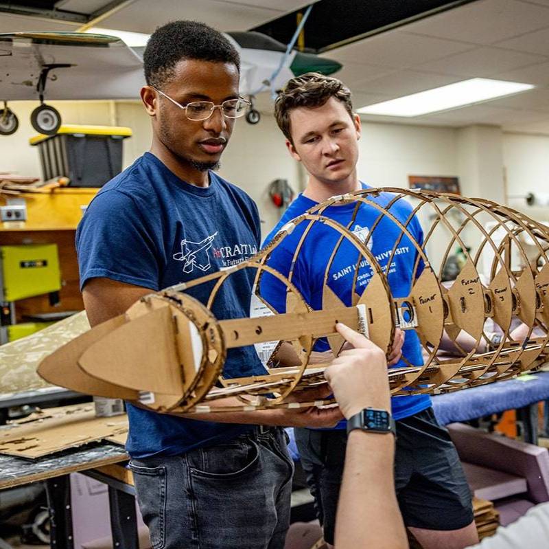 Two students stand next to each other while working on the frame of an aircraft.
