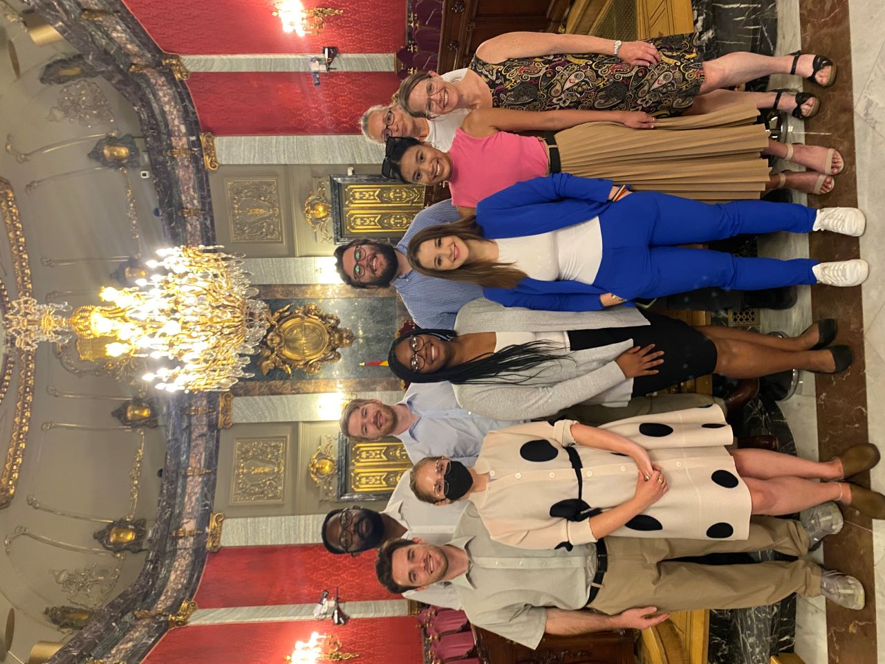 Students stand in an ornate courtroom with a large chandelier.