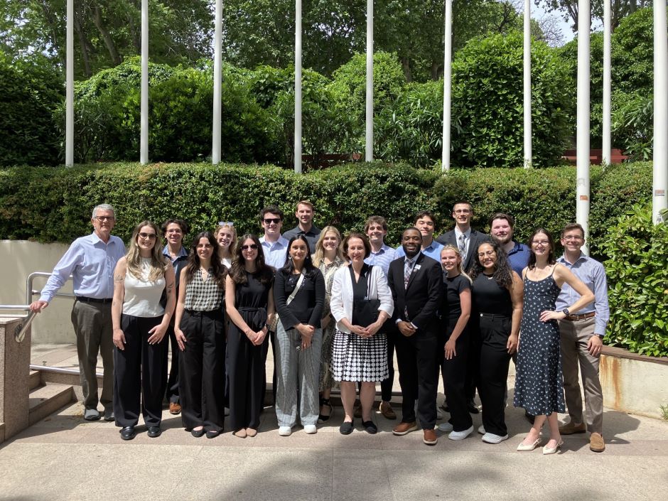 group of students and professors stand outdoors in front of some bushes
