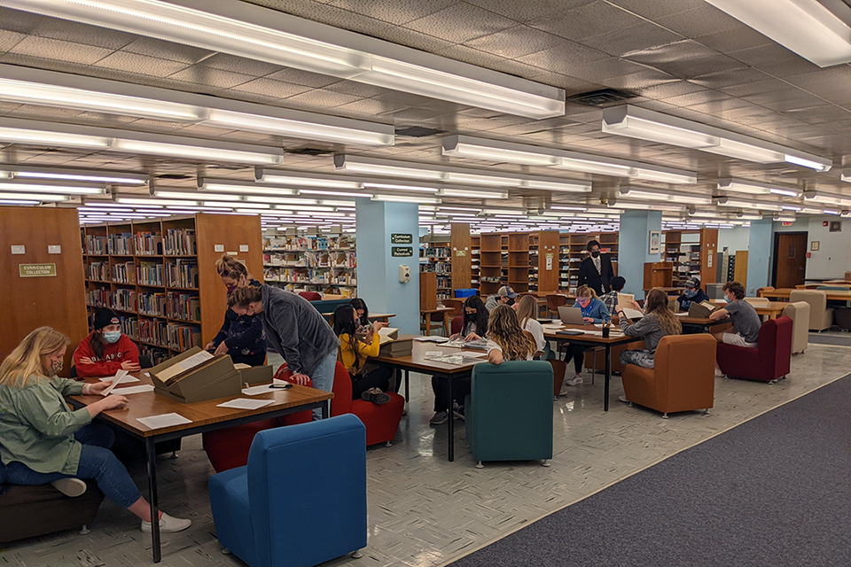 Students examine books while sitting at tables in a library.