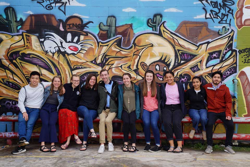 Immersion Program participants pose in front of a wall mural of cartoon character Sylvester the cat. 