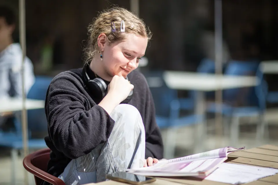 Student reading a book in a busy student area.