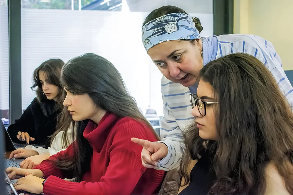 Computer class with a student and the teacher looking at a laptop.