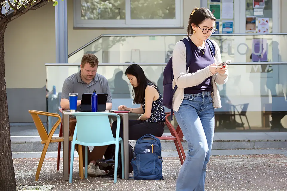 Students with a laptop looking at a phone in the patio of PRH.