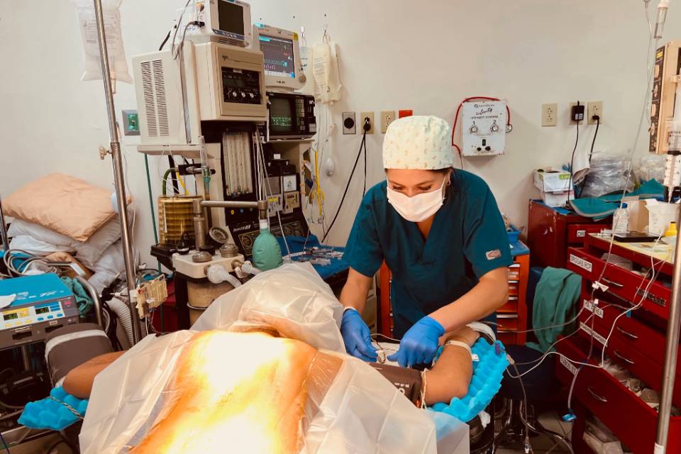 A doctor wearing scrubs, gloves and a surgical mask bends over a patient in an operating room