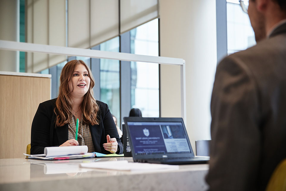 A healthcare management professional speaks to a table of healthcare professionals in a boardroom.