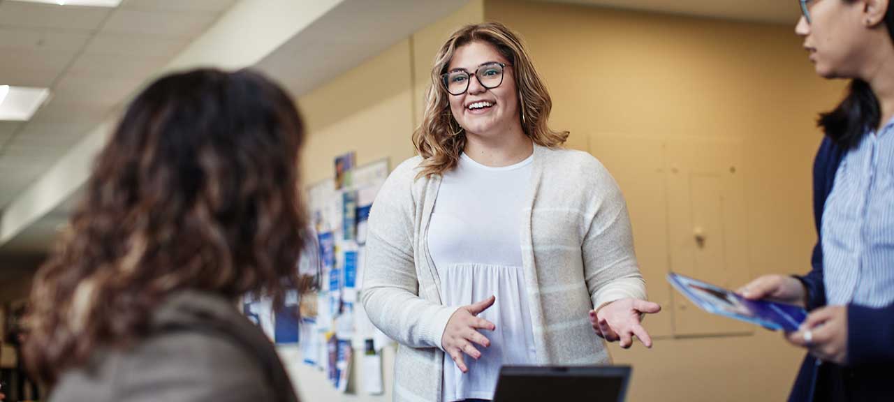 A woman speaks with two other women in a hallway at SLU's College for Public Health and Social Justice.